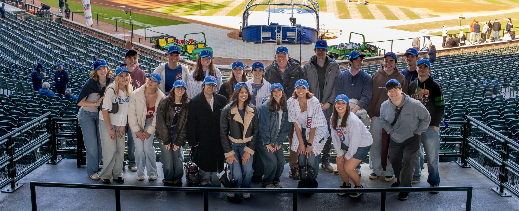 Large group of Loyola Media Fellows students posing together in the stands at Wrigley Field with the baseball field visible behind them.